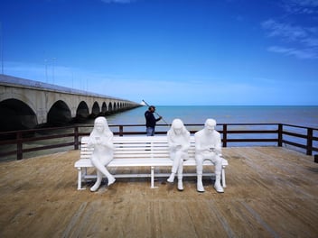 estatuas-sentadas-en-banco-de-malecón-en-día-espejado