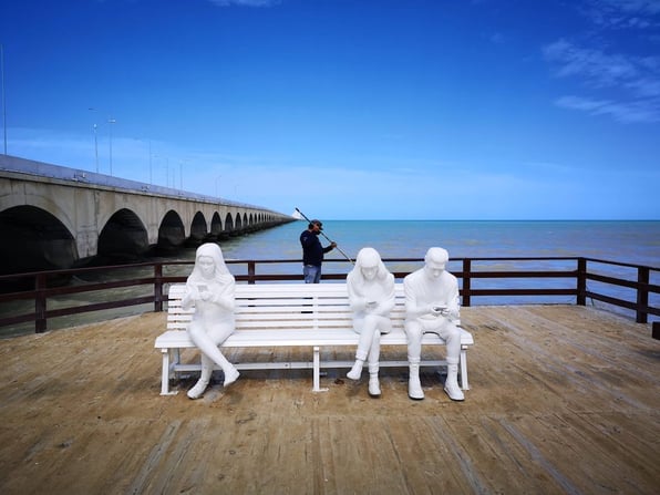 estatuas-sentadas-en-banco-de-malecón-en-día-espejado